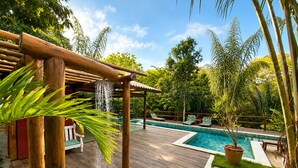 Una terrazza in legno con piscina, sedie a sdraio e un pergolato con elemento d'acqua.