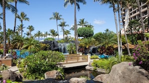 Ein tropisches Resort mit einem Wasserfall, Palmen und einer Brücke über einem kleinen Bach.