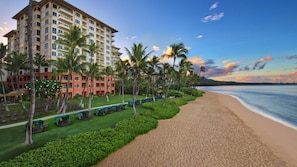 Ein Strandhotel mit mehreren Etagen, Palmen und einem Sandstrand.