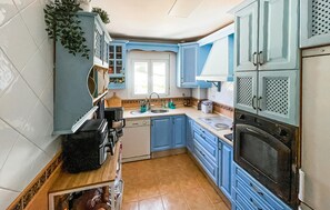 Cuina amb armaris blaus, un rentaplat, una placa de cocció i una finestra.