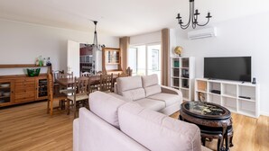 A modern living room with a sectional sofa, dining area with wooden furniture, a TV, and a globe on the wall. - Desassossego House | Swimming pool | Sauna | Peace and quiet (Monção)