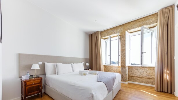 A hotel room with a large bed, wooden nightstand, and two windows with curtains. - Desassossego House | Swimming pool | Sauna | Peace and quiet (Monção)