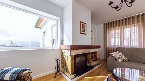 A living room with a fireplace, a sofa, a coffee table, and a view of mountains through a large window. - Desassossego House | Swimming pool | Sauna | Peace and quiet (Monção)