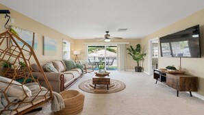 A spacious living room with a sofa, a hanging chair, a coffee table, and a TV mounted on the wall. - Your Resort Home! Walk to Disney & Beach! (Kapolei)