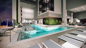 En modern inomhuspool med en glasvägg som avgränsning, solstolar och en grön vägg som dekorativt inslag.