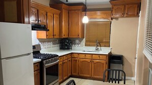 A kitchen with wooden cabinets, a refrigerator, a stove, and a dining table with chairs. - Beautiful 3-bedroom townhome with AC in charming Brownsville (Brownsville)