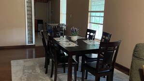 A dining area with a table set for six, surrounded by chairs, a ceiling fan, and a view of a kitchen and hallway. - Beautiful 3-bedroom townhome with AC in charming Brownsville (Brownsville)