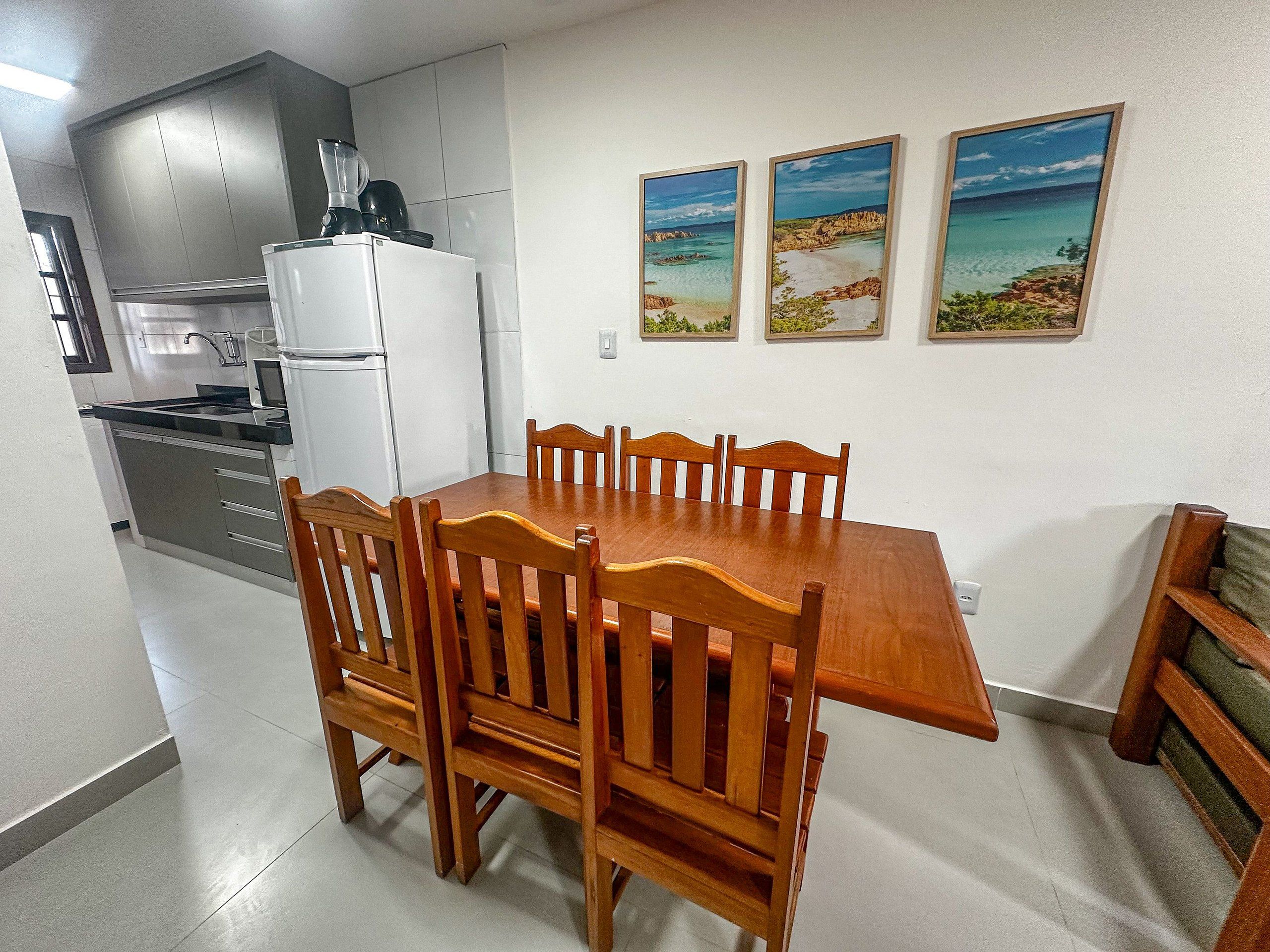A compact kitchen with a refrigerator, stove, and microwave. There is a wooden dining table with chairs. Three framed pictures are on the wall.