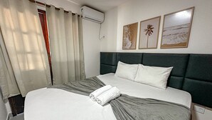 Un lit bien fait, avec une couette grise et blanche, une tête de lit sombre et un climatiseur fixé au mur.