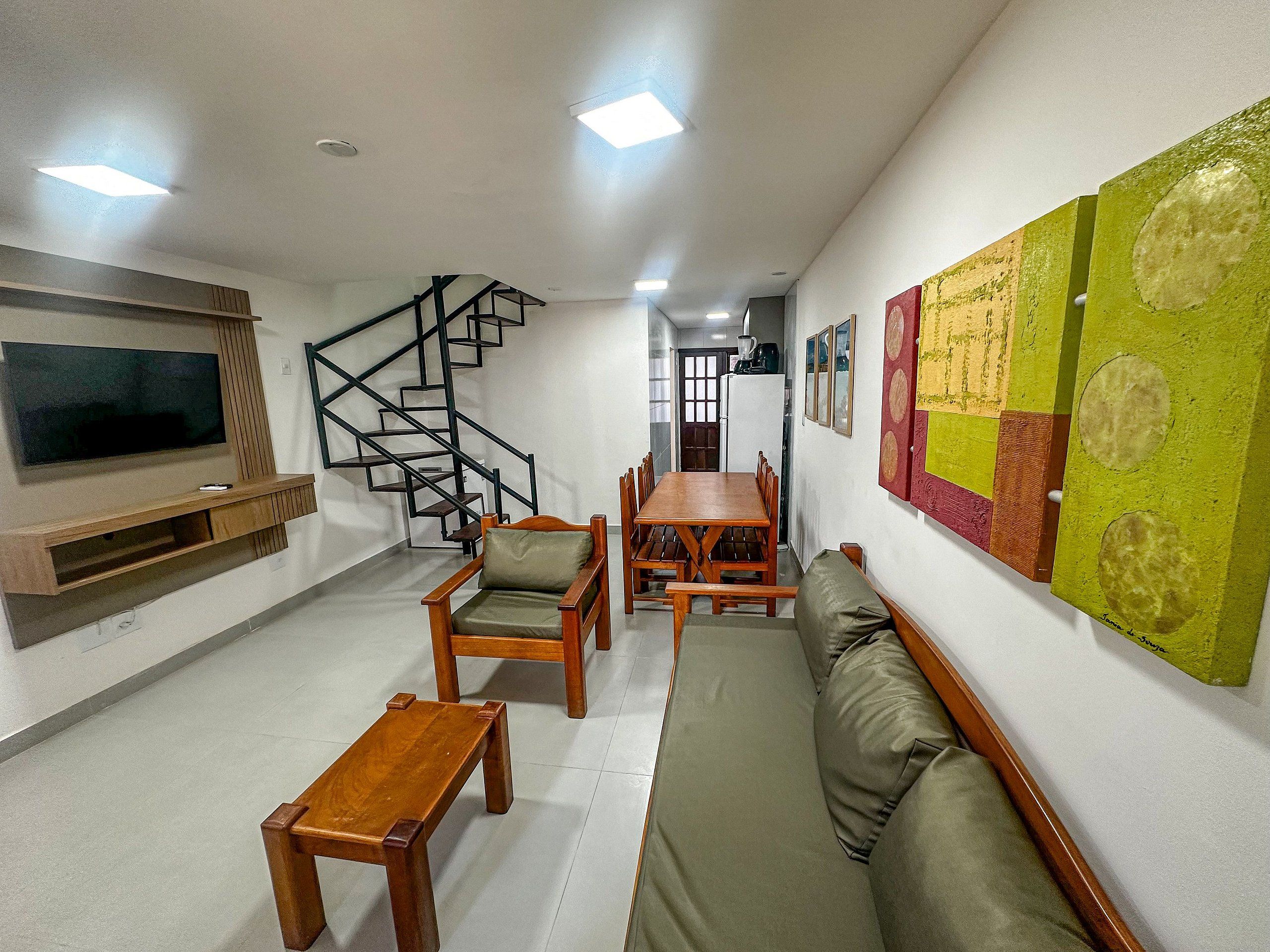 A living room with a TV, wooden furniture, a staircase, and a wall with artwork.