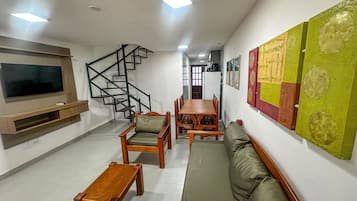 A living room with a TV, wooden furniture, a staircase, and a wall with artwork.