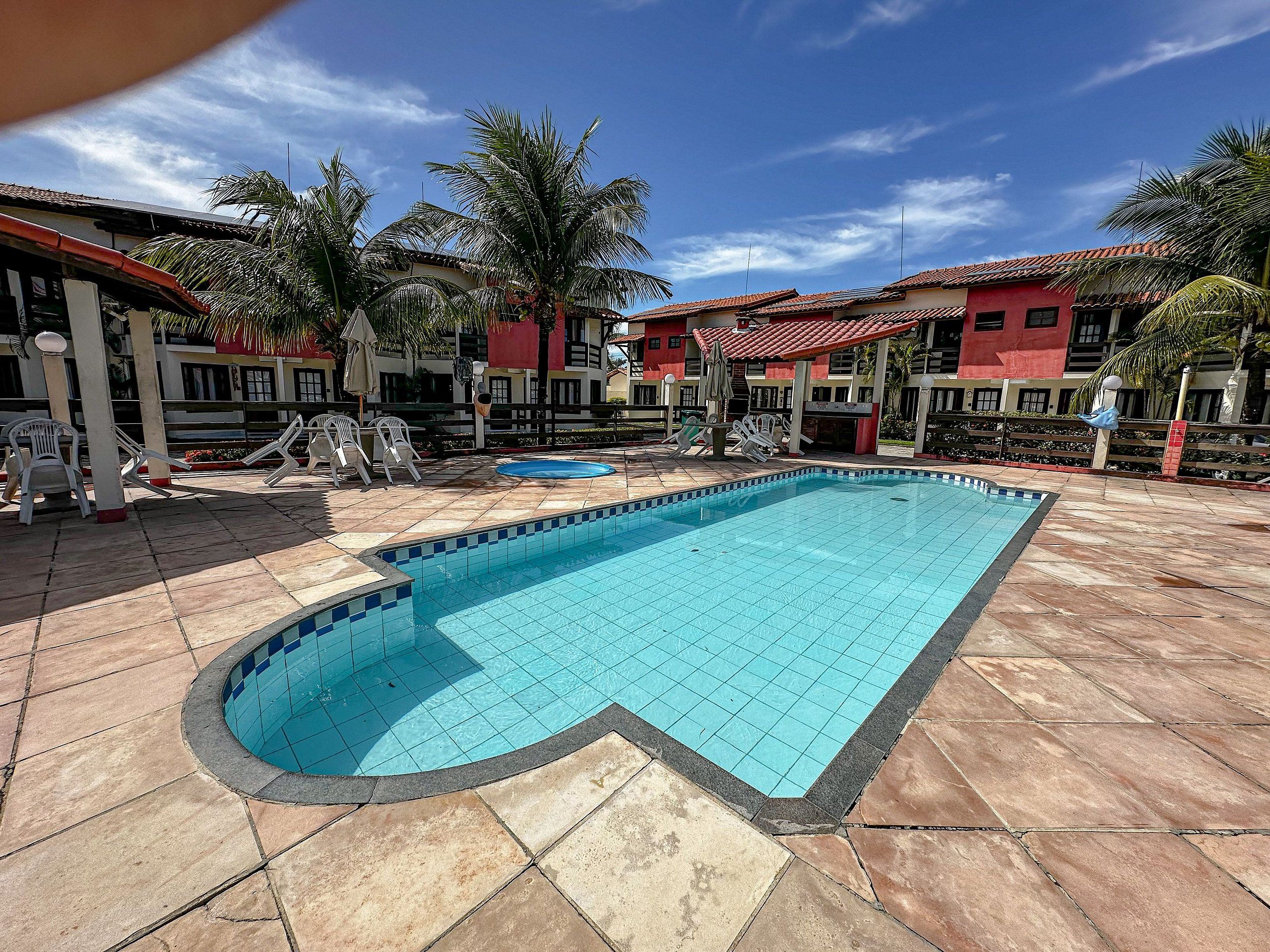 A swimming pool with tiled edges, surrounded by palm trees and red-roofed buildings.