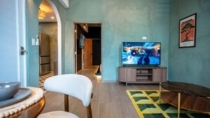 A modern living room with a television, a dining area with chairs, and a kitchen visible in the background. - Nichiyōbi House「UNIT #1「Koneko」 (San Juan)