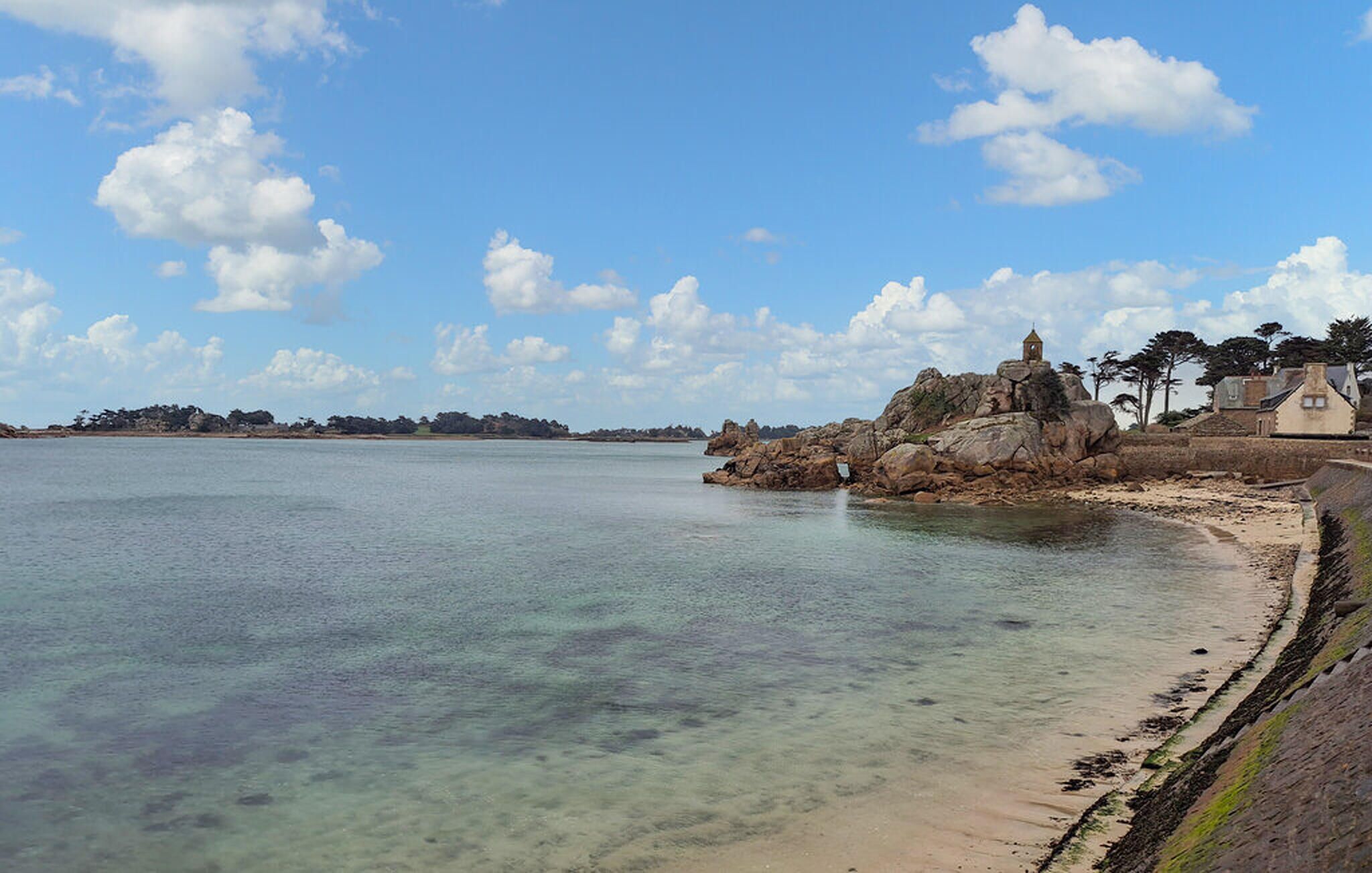 A coastal landscape with clear waters, a sandy beach, and rocky formations.
