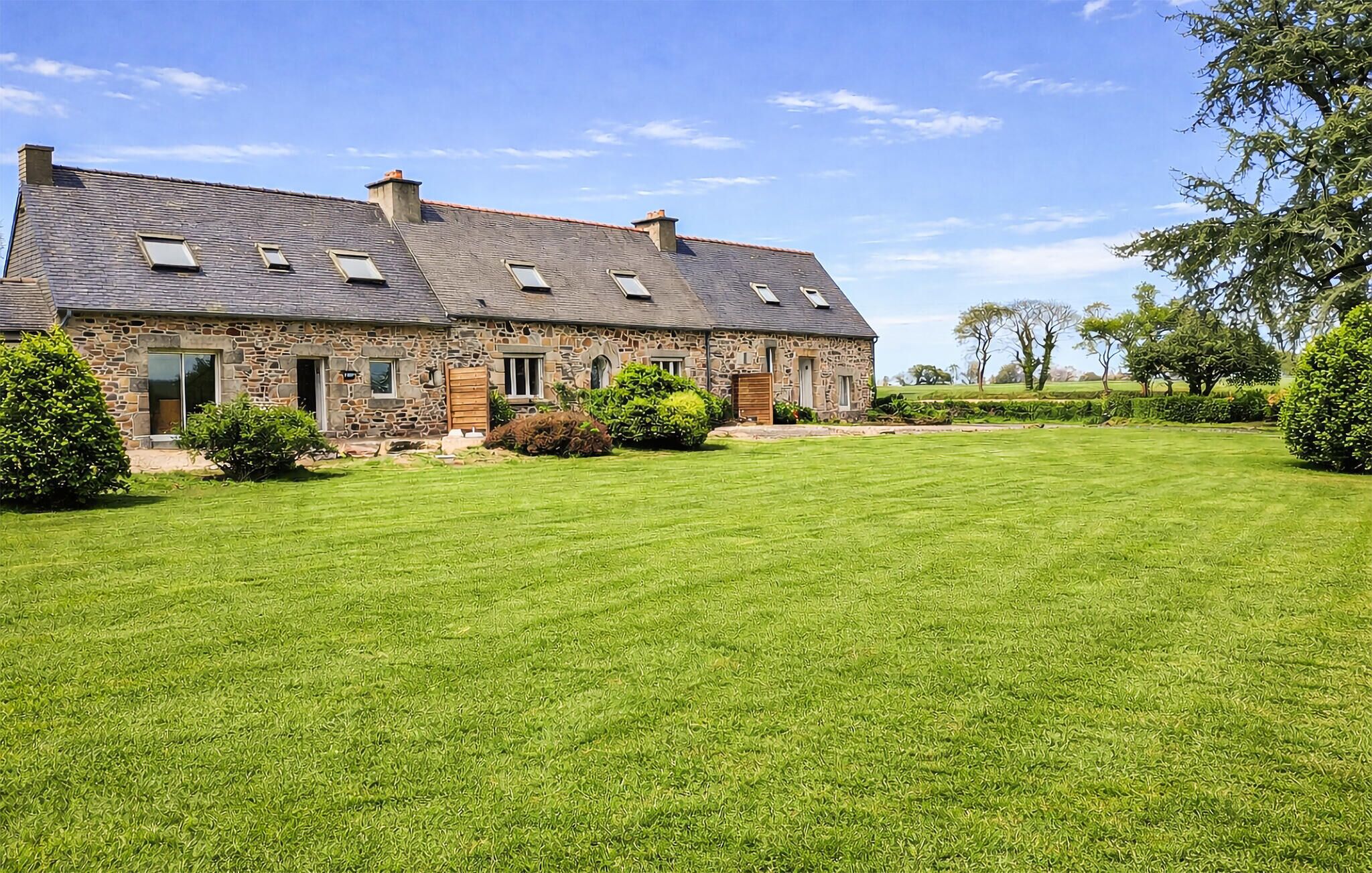 Une maison en pierre avec un toit en pente, de nombreuses fenêtres et une pelouse bien entretenue.
