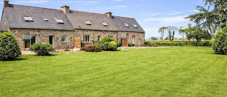 A stone house with a sloped roof, multiple windows, and a well-maintained lawn.