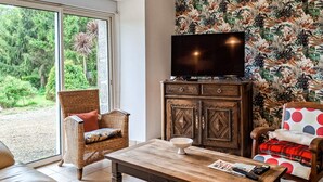Uma sala de estar com televisão sobre um móvel, uma cadeira de vime, uma mesa com uma tigela e uma cadeira com bolinhas.