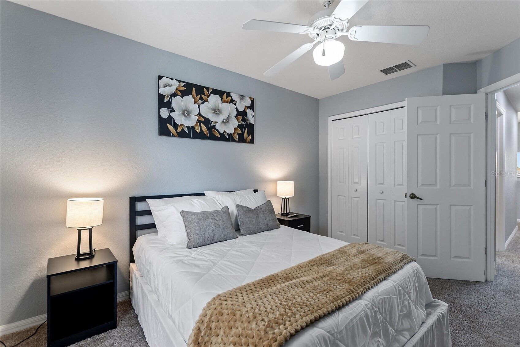 A bedroom with a bed, two bedside tables with lamps, a ceiling fan, and a door.