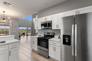 A modern kitchen with stainless steel appliances, white cabinetry, and a large island. - A spacious and updated home with pool, minutes from Disney, golf, and more. (Davenport)