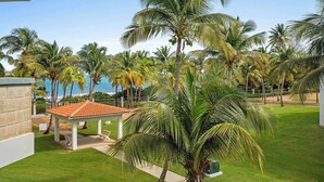 En resort med en palmelindet sti, der fører til en pavillon med et flisbelagt tag, med udsigt over havet.