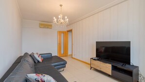 A modern living room with a large flat-screen TV, a dark leather sofa, and a wooden entertainment unit. - Camilo Apartment - By Y Concept (Setúbal)