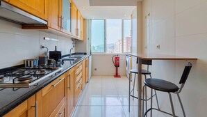 A modern kitchen with wooden cabinets, a gas stove, and a window overlooking a cityscape. - Camilo Apartment - By Y Concept (Setúbal)