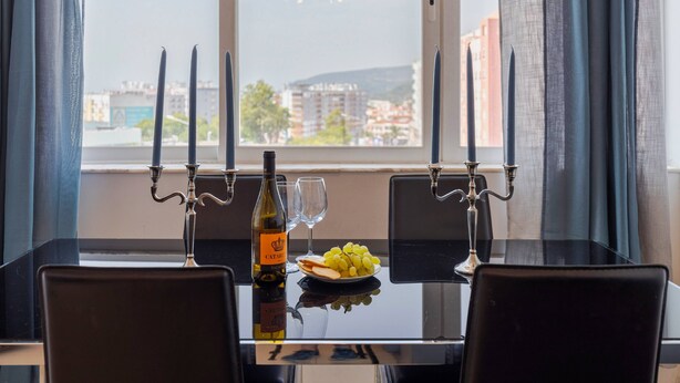 A dining table with a bottle of wine, a glass, and a plate of grapes. - Camilo Apartment - By Y Concept (Setúbal)