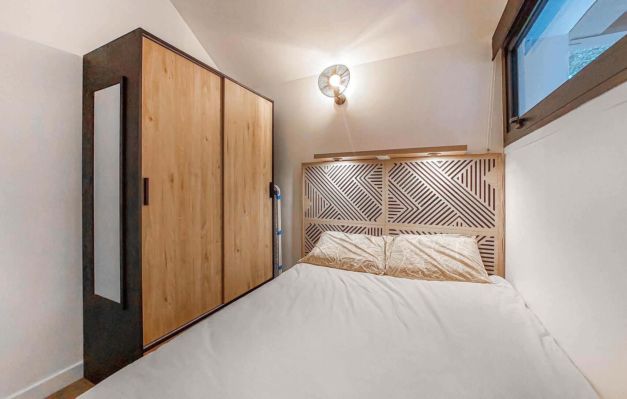 Un dormitorio con cama, armario de madera y lámpara fijada a la pared.
