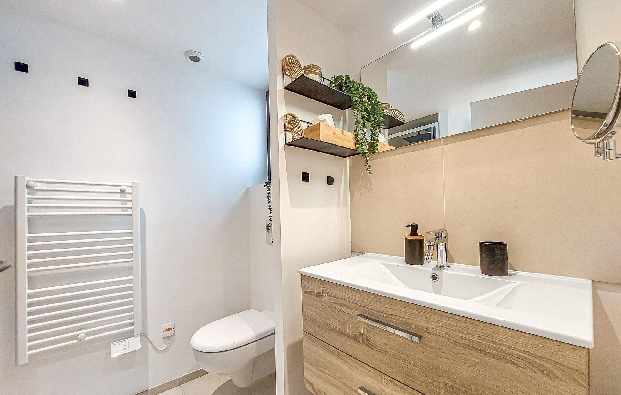 A modern bathroom with a white toilet, a white sink with a wooden vanity, a mirror, and a towel rack.