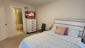 Ein Schlafzimmer mit Bett, Fernseher, Kommode und einer Tür zu einem Badezimmer.