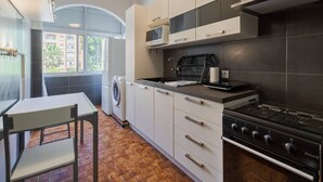 A modern kitchen with white cabinets, a gas stove, a microwave, and a washing machine. - Lisboa no Sado - By Y Concept (Setúbal)