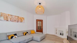 A modern living room with a grey sectional sofa, a woven pendant light, a wooden door, and a wall-mounted TV. - Lucia House - By Y Concept (Setúbal)