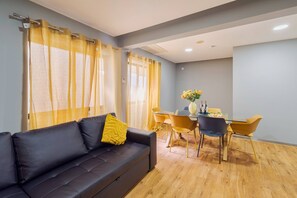 A modern living room with a sofa, dining table, chairs, and curtains.