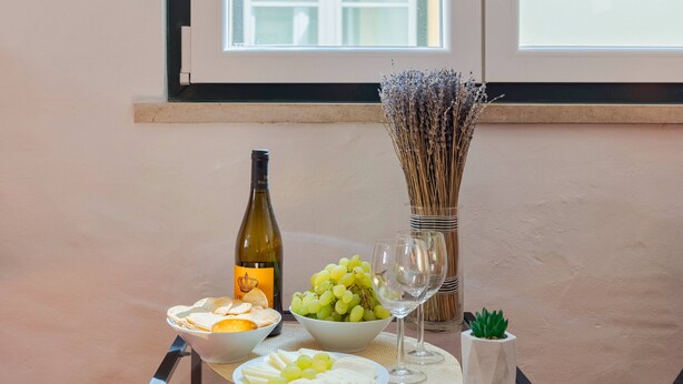 Una mesa con una botella de vino, cuencos de uvas y queso, y un jarrón de flores secas.