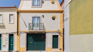 Un edificio de dos pisos con una puerta verde, un balcón con barandilla de metal y una ventana pequeña sobre la puerta.