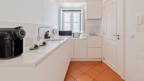 Una cocina compacta con armarios blancos, cafetera, hervidor y juego de té.
