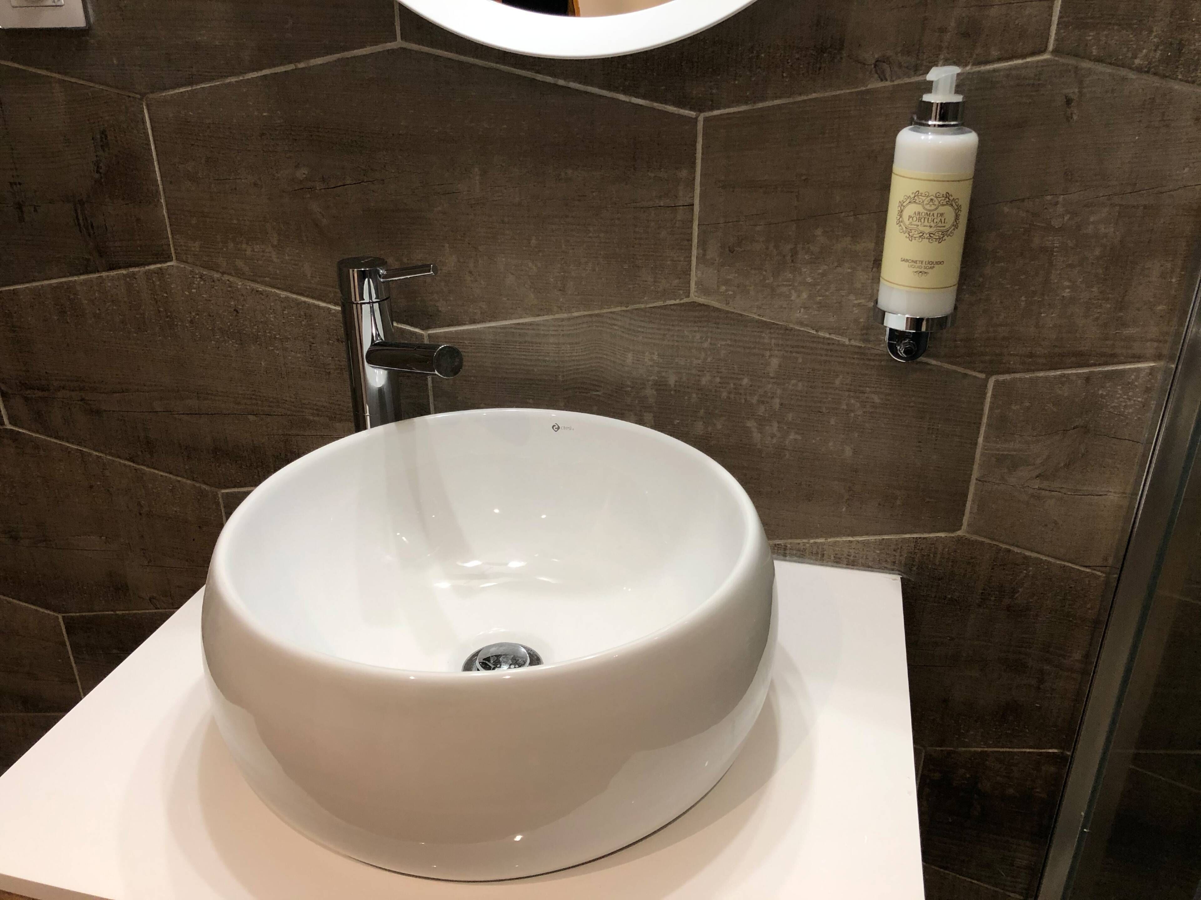 A bathroom with a white sink, a mirror, and a soap dispenser on the wall.