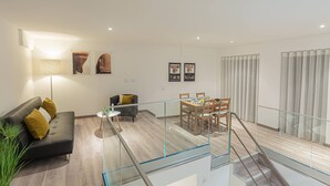 Una sala de estar moderna con barandilla de vidrio, un sofá con cojines, una mesa de comedor con sillas y obras de arte en las paredes.
