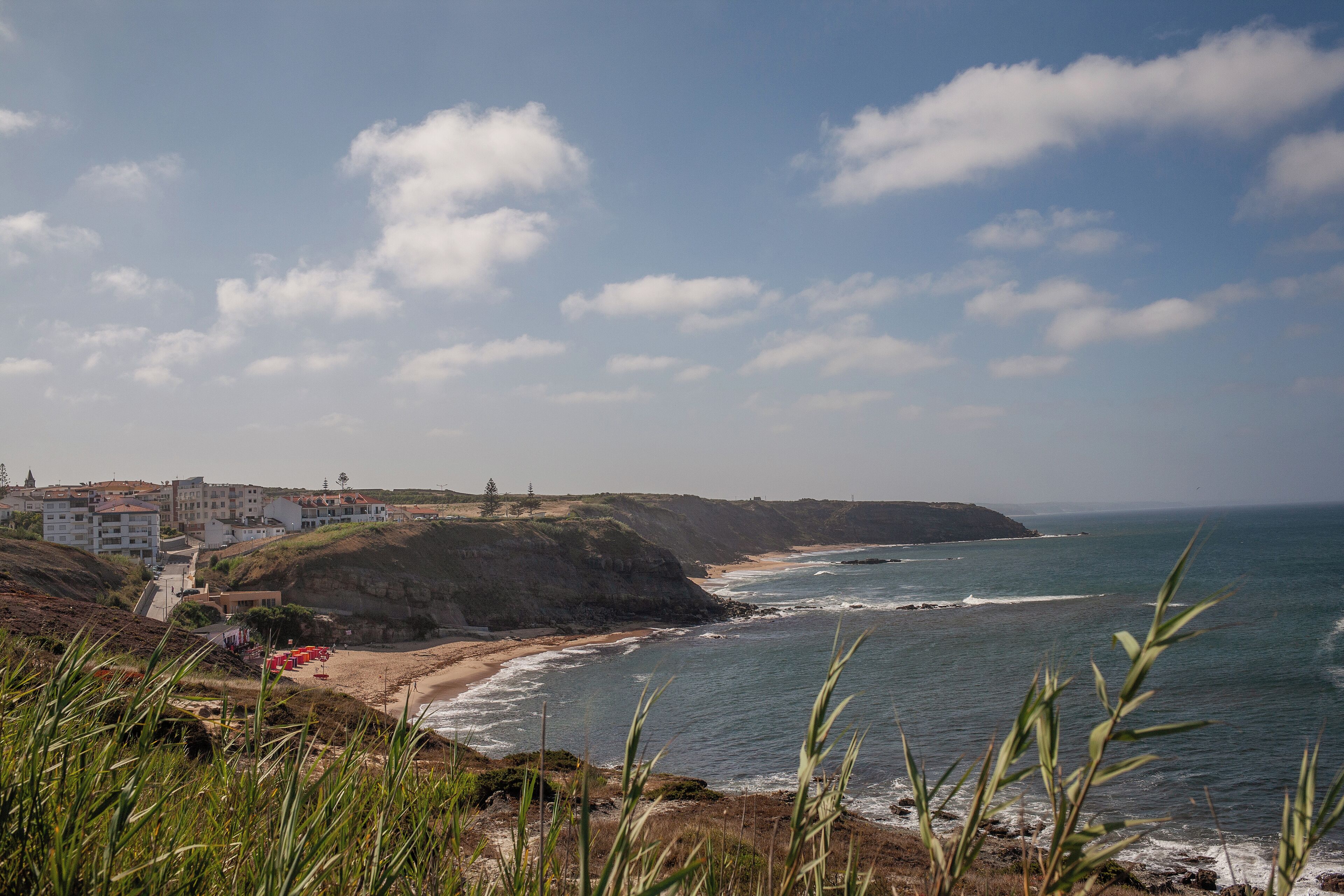 A coastal landscape with buildings on a hillside, a beach, and the ocean.