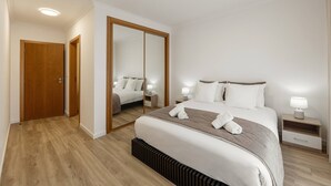 Moderni hotellihuone, jossa on suuri sänky, puinen vaatekaappi, peili ja yöpöytä, jossa on lamppu.