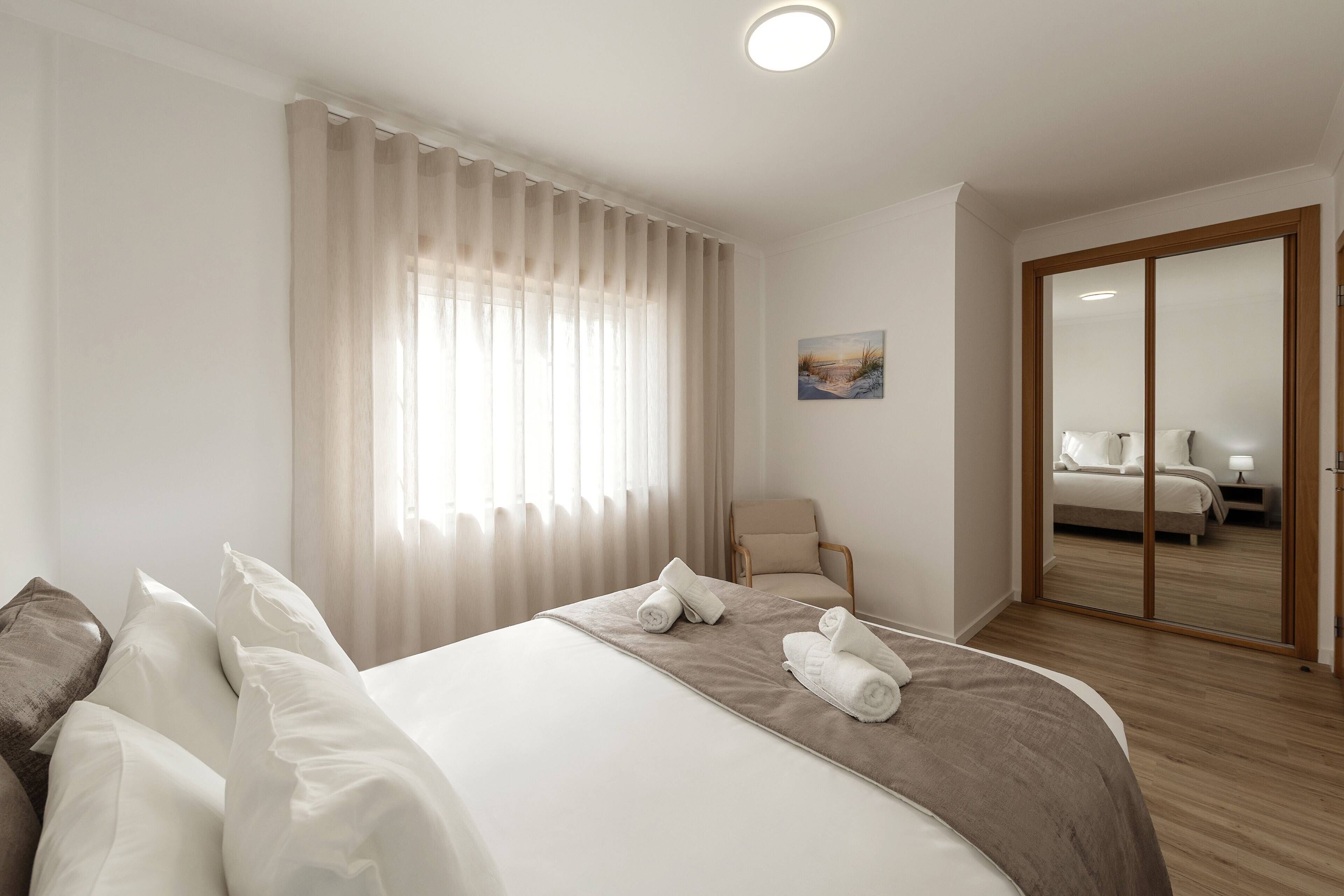 A hotel room with a bed, a chair, a painting, and a sliding door leading to another room.