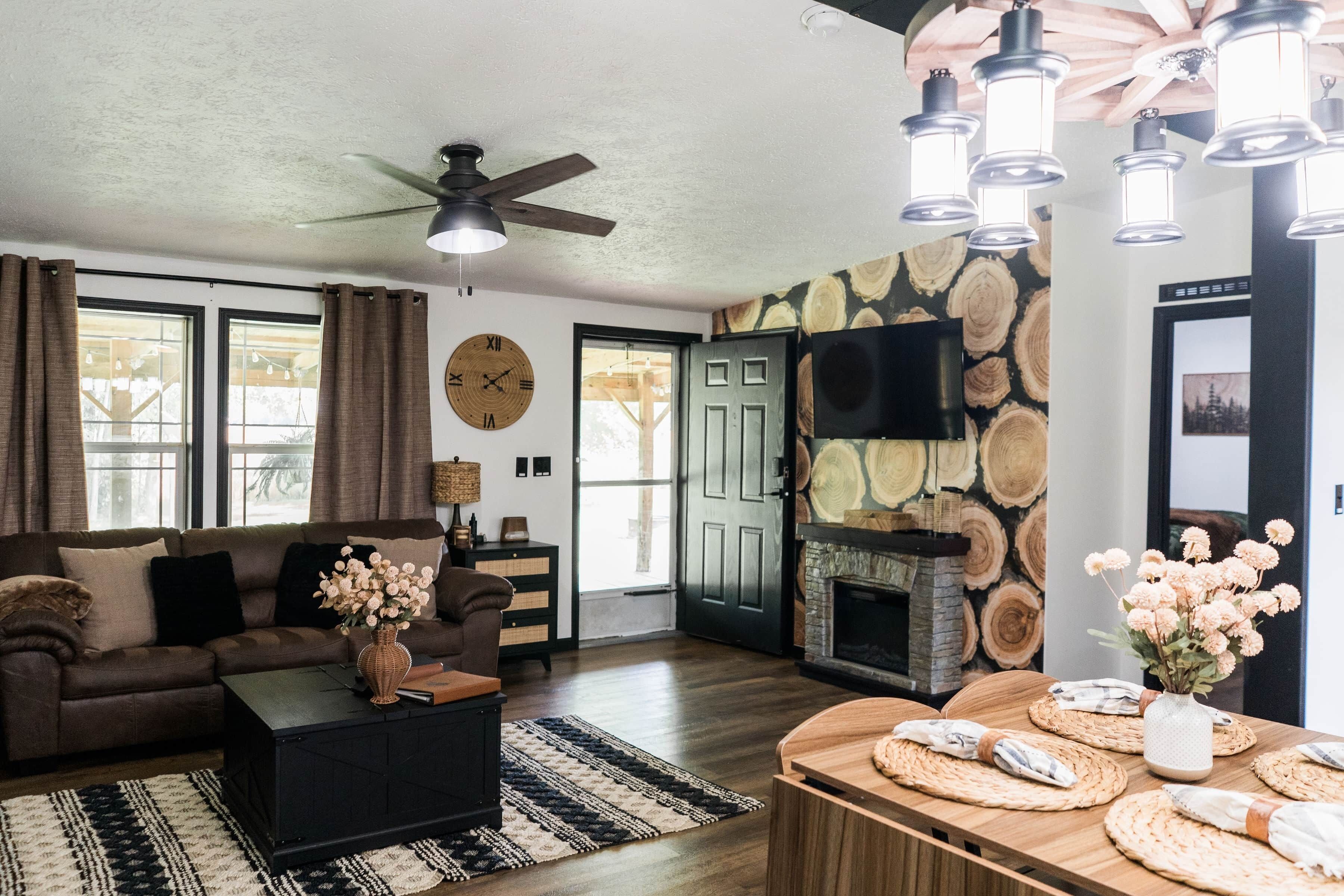 Una sala de estar con sofá, mesa de centro y chimenea. Hay un reloj en la pared y una puerta que conduce a otra habitación.