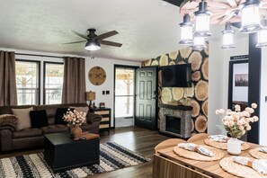 Una sala de estar con sofá, mesa de centro y chimenea. Hay un reloj en la pared y una puerta que conduce a otra habitación.