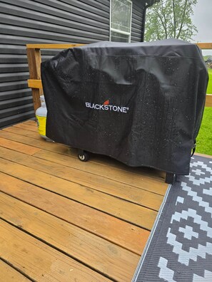 Un barbecue couvert, muni de roulettes, installé sur une terrasse en bois.