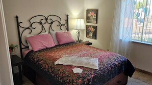 A bed with a floral bedspread, two pink pillows, a white knitted blanket, and a nightstand with a lamp and a tissue box. - Beautiful 2-bedroom Golf house in Green Valley perfect for relaxing getaway (Green Valley)