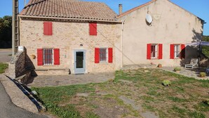 Un bâtiment en pierre avec des volets rouges et un toit en tuiles.