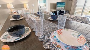 A dining table set with glassware and plates, a television, and a sofa in a room with a view.