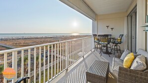 A balcony with wicker furniture, a view of the beach, and a sign for Dauphin Island Stays.