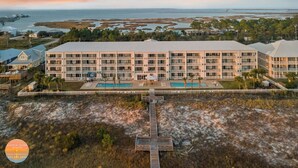 A large resort with multiple balconies, a pool area, and a pier leading to the beach.