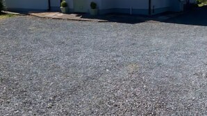 Una casa de dos plantas con techo gris, paredes blancas y camino de entrada de grava.